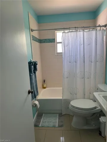 Full bathroom with toilet, shower / tub combo with curtain, and tile patterned flooring