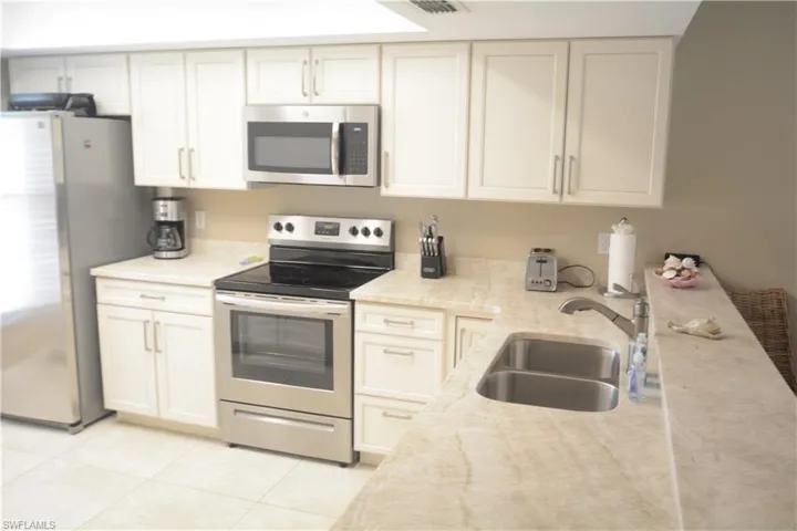 Kitchen featuring appliances with stainless steel finishes, light tile patterned floors, a sink, and light stone counters