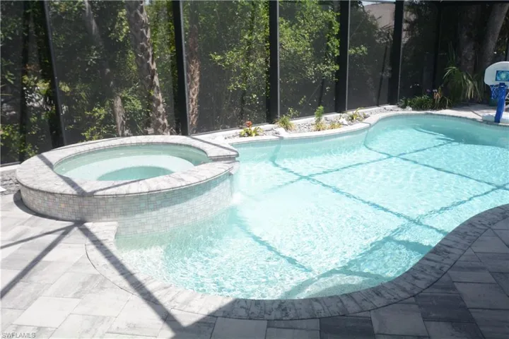 View of pool with a pool with connected hot tub, a patio area, and glass enclosure