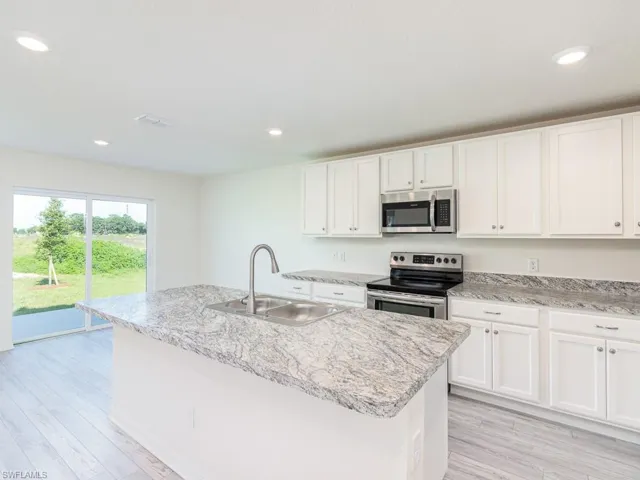 Kitchen with stainless steel appliances, white cabinetry, recessed lighting, an island with sink, and light stone countertops