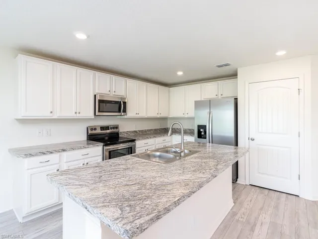 Kitchen with stainless steel appliances, white cabinetry, light wood-style flooring, light countertops, and recessed lighting