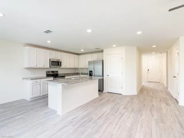 Kitchen featuring appliances with stainless steel finishes, light stone counters, a center island with sink, white cabinets, and light wood finished floors