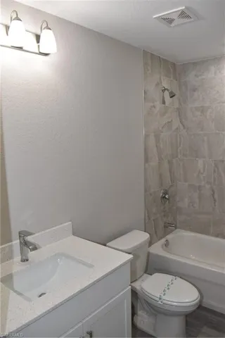 Full bathroom with a textured ceiling, tiled shower / bath, toilet, vanity, and wood-type flooring