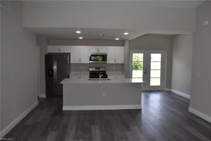 Kitchen with dark wood-type flooring, stainless steel appliances, and a kitchen island with sink