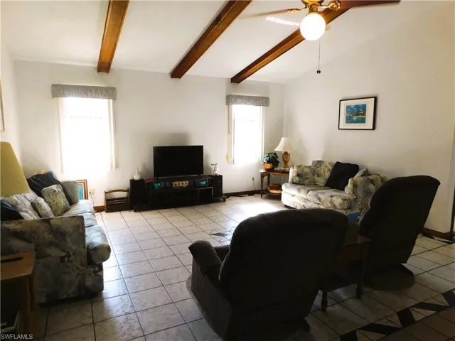 Tiled living room featuring ceiling fan and vaulted ceiling with beams and Smart TV