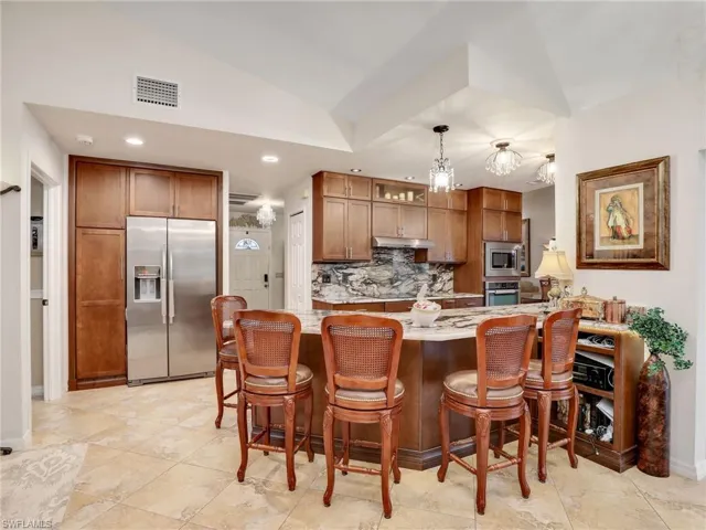 Kitchen with stainless steel appliances, decorative backsplash, pendant lighting, a breakfast bar area, and vaulted ceiling