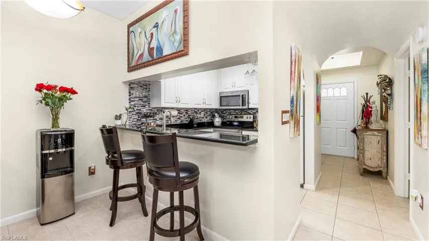 Kitchen featuring light tile patterned floors, white cabinetry, tasteful backsplash, arched walkways, and stainless steel appliances