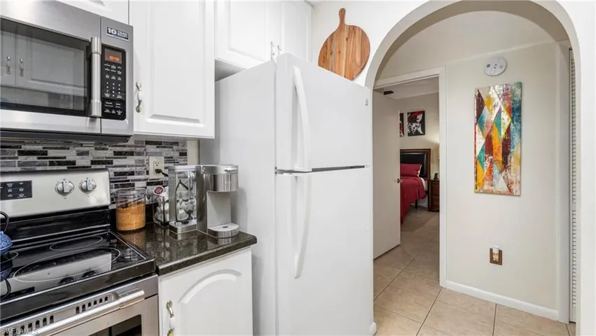 Kitchen featuring stainless steel appliances, white cabinetry, dark stone counters, arched walkways, and light tile patterned floors