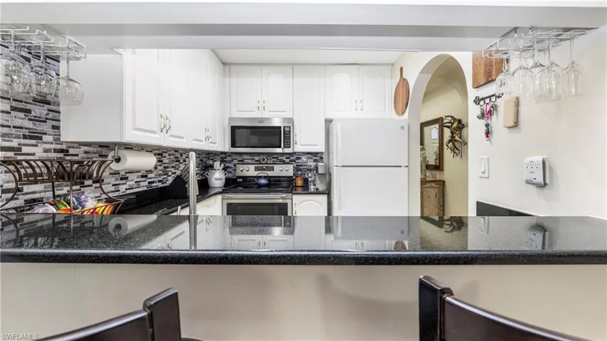 Kitchen featuring white cabinetry, stainless steel appliances, dark stone counters, backsplash, and arched walkways
