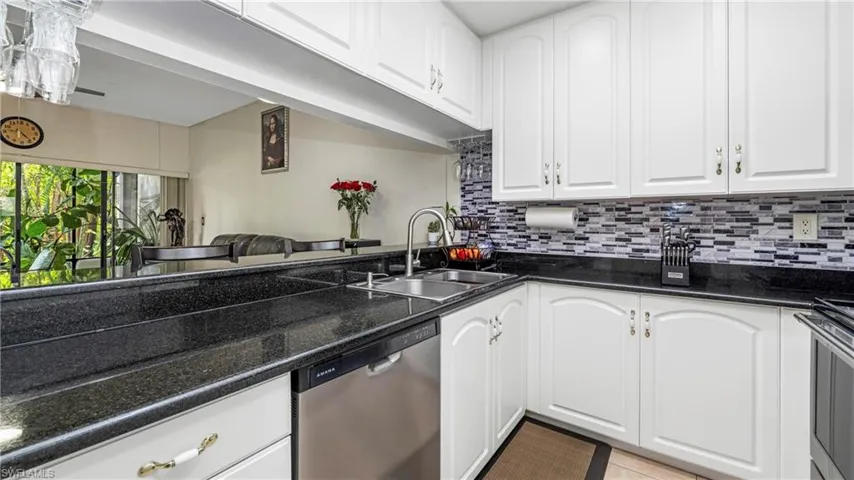 Kitchen featuring dark stone countertops, white cabinetry, stainless steel appliances, and tasteful backsplash