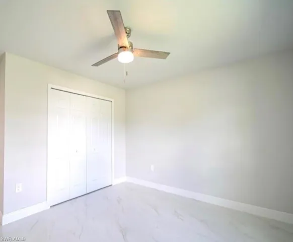 Interior space featuring light gray walls, a ceiling fan with light fixture, white bi-fold closet doors, white baseboards, and light-toned tile flooring