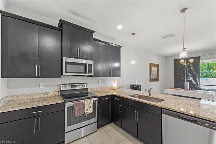 Kitchen featuring stainless steel appliances, light stone countertops, dark cabinetry, pendant lighting, and light tile patterned flooring