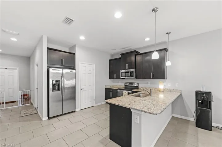 Kitchen featuring stainless steel appliances, light stone countertops, a peninsula, decorative light fixtures, and a breakfast bar