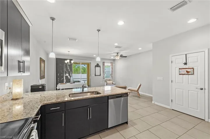 Kitchen featuring dark cabinetry, a peninsula, stainless steel appliances, light stone countertops, and hanging lights