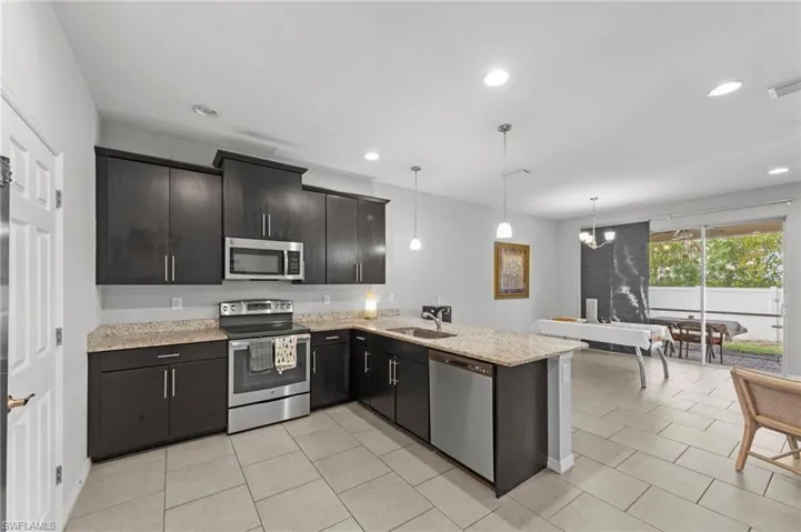 Kitchen with stainless steel appliances, a peninsula, hanging light fixtures, light stone countertops, and light tile patterned floors