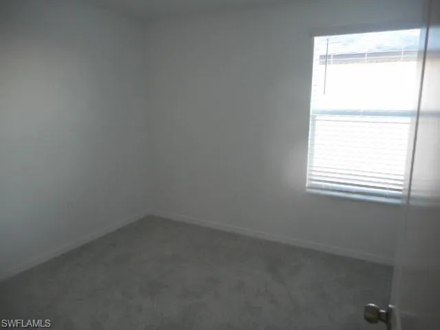 Spare room featuring dark carpet and baseboards