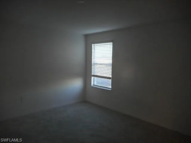Empty room featuring dark carpet and baseboards