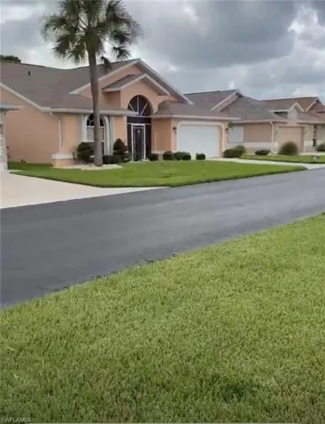 Exterior featuring a light peach stucco finish, arched entry, single palm tree, attached garage, and a manicured lawn