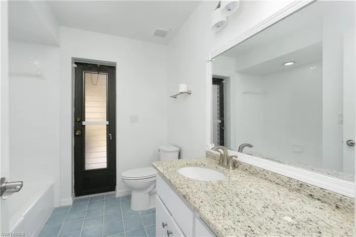 Full bath with toilet, tile patterned flooring, visible vents, and vanity with granite counter. Freshly painted interior.
