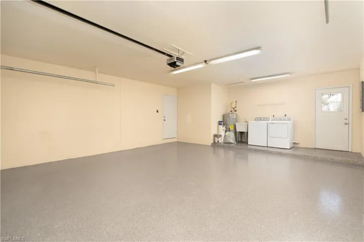 Garage featuring a garage door opener, electric water heater, and washer and clothes dryer. Freshly painted and with new epoxy flooring.
