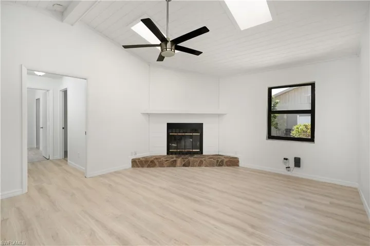 Family room with floorboards, a glass covered fireplace, lofted ceiling with skylight, ceiling fan, and Pergo flooring.  Freshly painted interior.