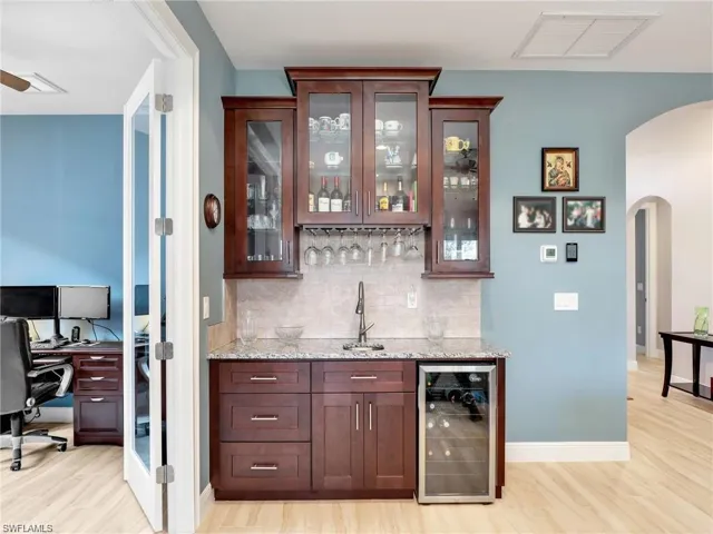 Bar featuring beverage cooler, light hardwood / wood-style floors, light stone counters, sink, and tasteful backsplash