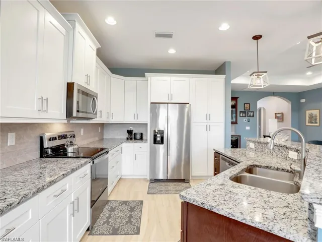 Kitchen featuring pendant lighting, stainless steel appliances, backsplash, white cabinets, and sink