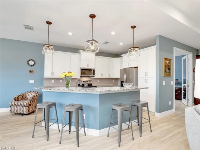 Kitchen with white cabinetry, a kitchen bar, backsplash, light stone countertops, and appliances with stainless steel finishes