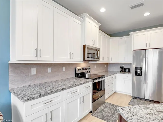 Kitchen with stainless steel appliances, white cabinetry, light stone counters, light hardwood / wood-style floors, and decorative backsplash