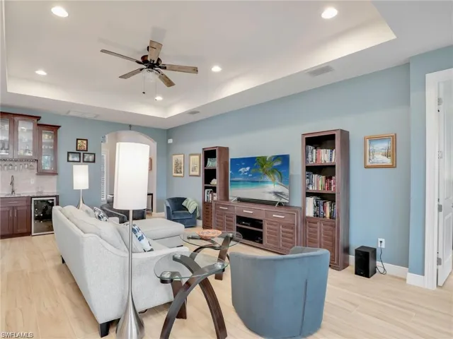 Living room with beverage cooler, a raised ceiling, light hardwood / wood-style flooring, and wet bar