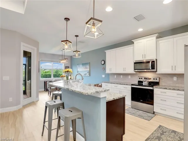 Kitchen with white cabinetry, backsplash, hanging light fixtures, a kitchen island with sink, and appliances with stainless steel finishes