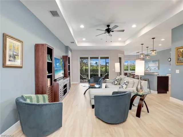 Living room with a raised ceiling, ceiling fan, and light hardwood / wood-style flooring