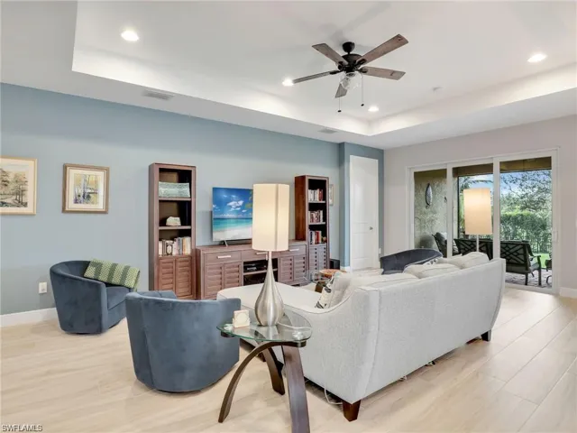 Living room with light wood-type flooring, ceiling fan, and a tray ceiling