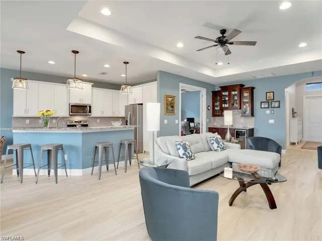 Living room with sink, ceiling fan, a tray ceiling, and light hardwood / wood-style flooring
