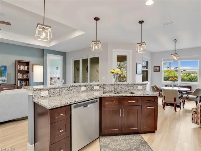 Kitchen featuring stainless steel dishwasher, light stone counters, and hanging light fixtures