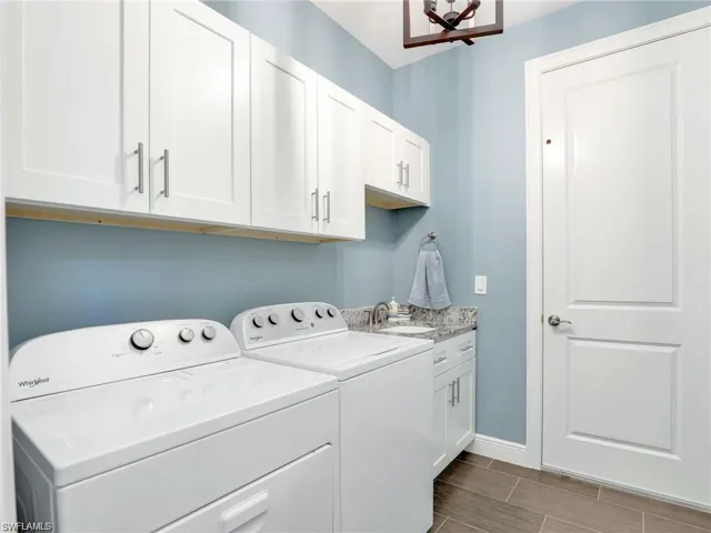 Clothes washing area featuring sink, cabinets, and washing machine and clothes dryer