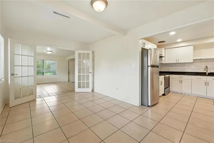 Kitchen featuring open shelves, dark countertops, stainless steel appliances, light tile patterned floors, and beamed ceiling