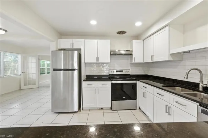 Kitchen with stainless steel appliances, light tile patterned floors, white cabinets, and decorative backsplash
