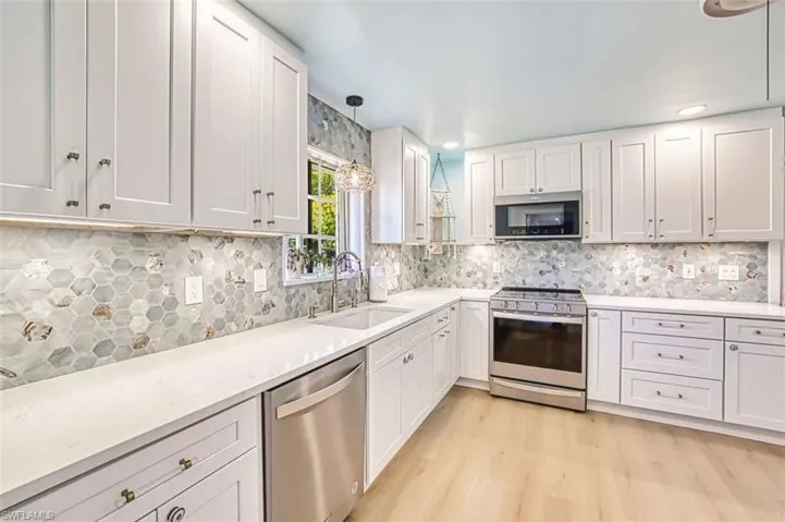 Newly updated kitchen with stainless steel appliances, pendant lighting, light wood-style flooring, quartz counters, and white wood cabinetry
