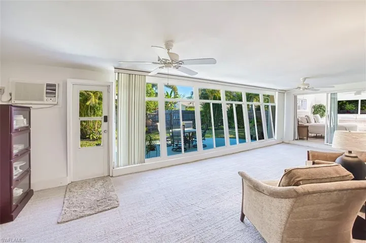 Sunroom featuring an AC wall unit and 2 ceiling fans with a wall of windows overlooking the lucious back yard