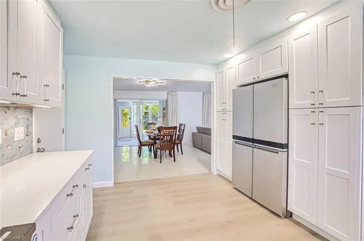 Kitchen with freestanding refrigerator, white cabinets, light wood finished floors, decorative backsplash, and recessed lighting