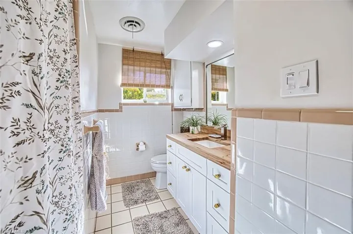 Guest bath with vanity, tile walls, light tile patterned flooring, and a shower with shower curtain