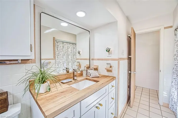 Guest bathroom featuring vanity, tile walls, a shower with curtain, light tile patterned floors, and a wainscoted wall