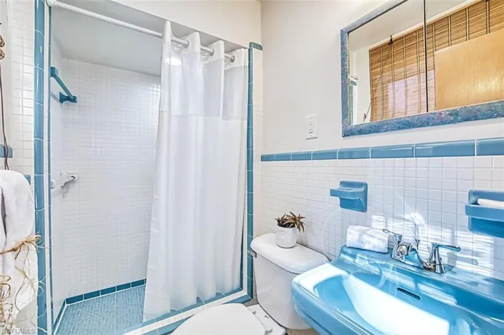 PrimaryBathroom featuring tile walls, a stall shower, and a wainscoted wall in Mid-Century Modern style.