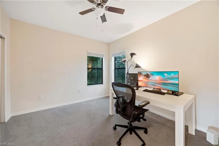 Carpeted home office featuring a ceiling fan and baseboards