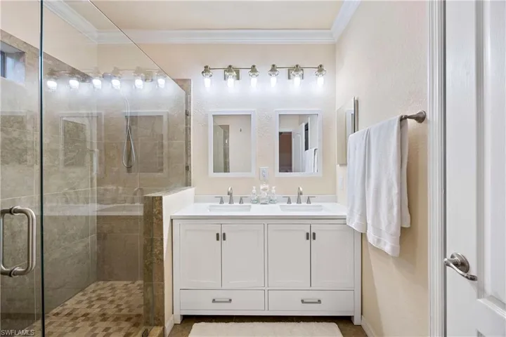 Full bathroom featuring ornamental molding, a shower stall, and double vanity