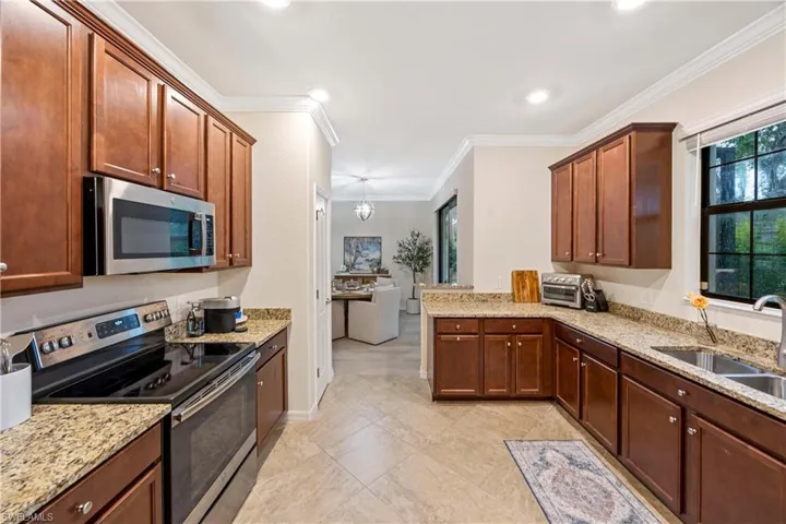 Kitchen featuring stainless steel appliances, ornamental molding, light stone counters, recessed lighting, and a peninsula