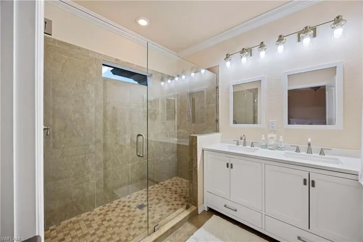 Full bath featuring ornamental molding, a shower stall, and double vanity