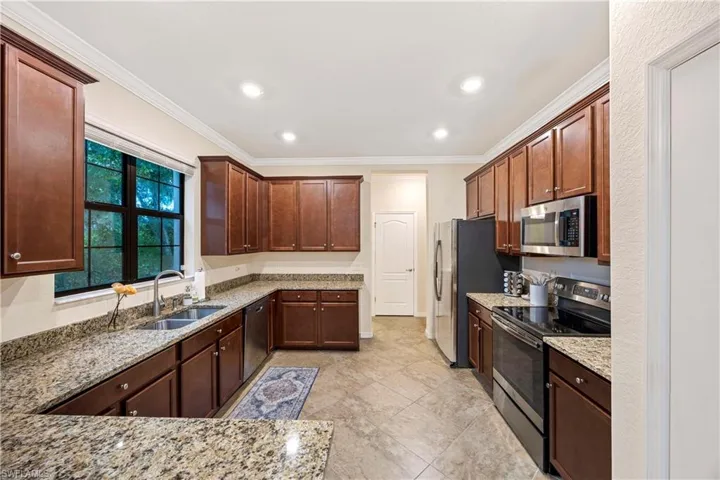 Kitchen featuring stainless steel appliances, light stone counters, crown molding, recessed lighting, and light tile patterned flooring