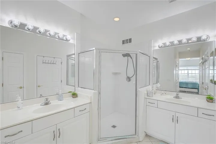 Full bath featuring ensuite bathroom, a stall shower, two vanities, light tile patterned floors, and recessed lighting
